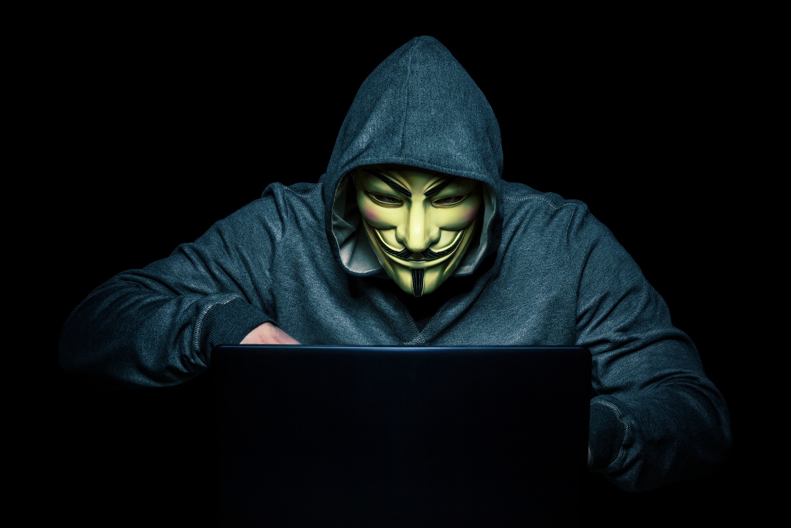 MILAN,ITALY, February, 2018: Hacker wears anonymus mask with notebook in the dark .