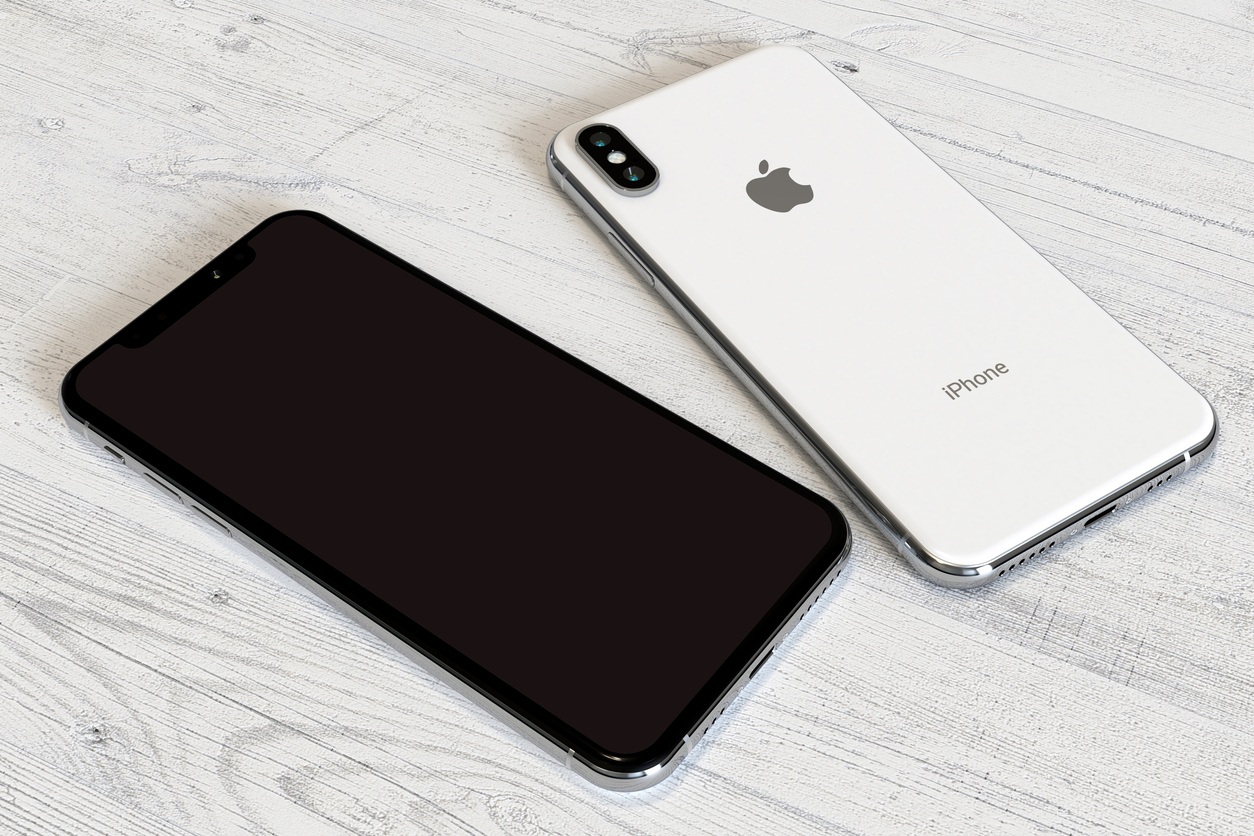 Apple iPhone XS Silver smartphone, comparison of the front side (screen) and the back side (camera) side by side, on a white wood surface. White OLED screen.Commercial editorial image, high angle perspective.