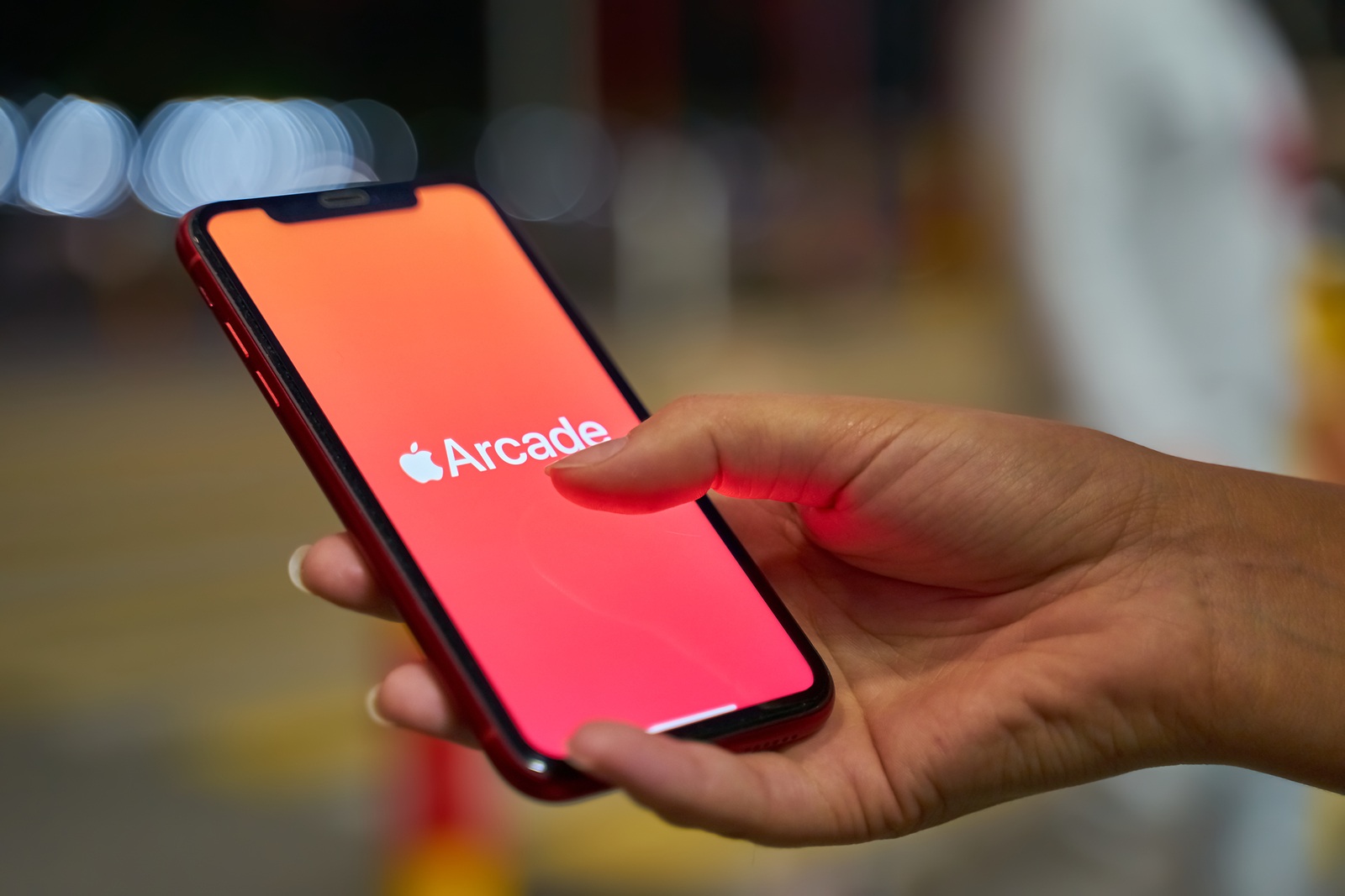 Bishkek, Kyrgyzstan - September 19, 2019: Woman holds the new iPhone in portrait mode and subscribes to apple arcade with orange background