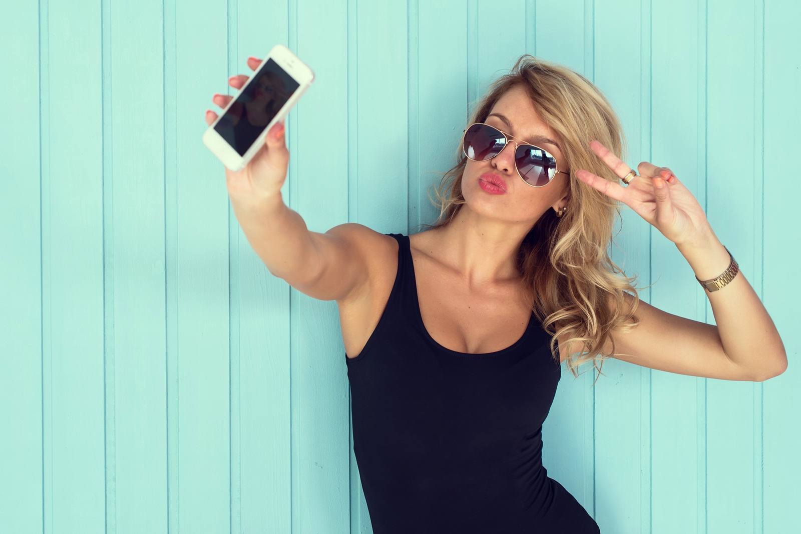 blonde woman in bodysuit with perfect body taking selfie with smartphone toned instagram filter