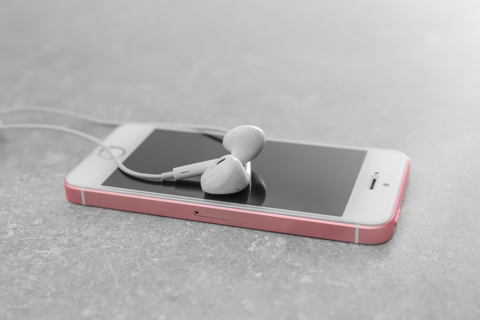 KIEV, UKRAINE - OCTOBER 12, 2017: Modern iPhone SE Rose Gold with earphones on gray background