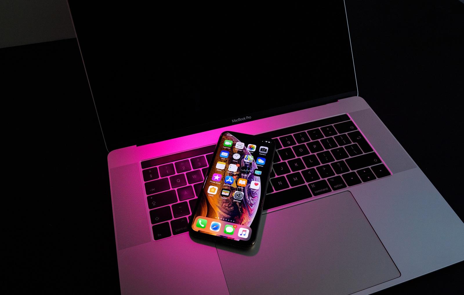 PARIS, FRANCE - SEP 25, 2018: New iPhone Xs and Xs Max smartphone model by Apple Computers close up. Newest golden Apple Iphone on pink magenta light on Macbook Pro 15 laptop keyboard