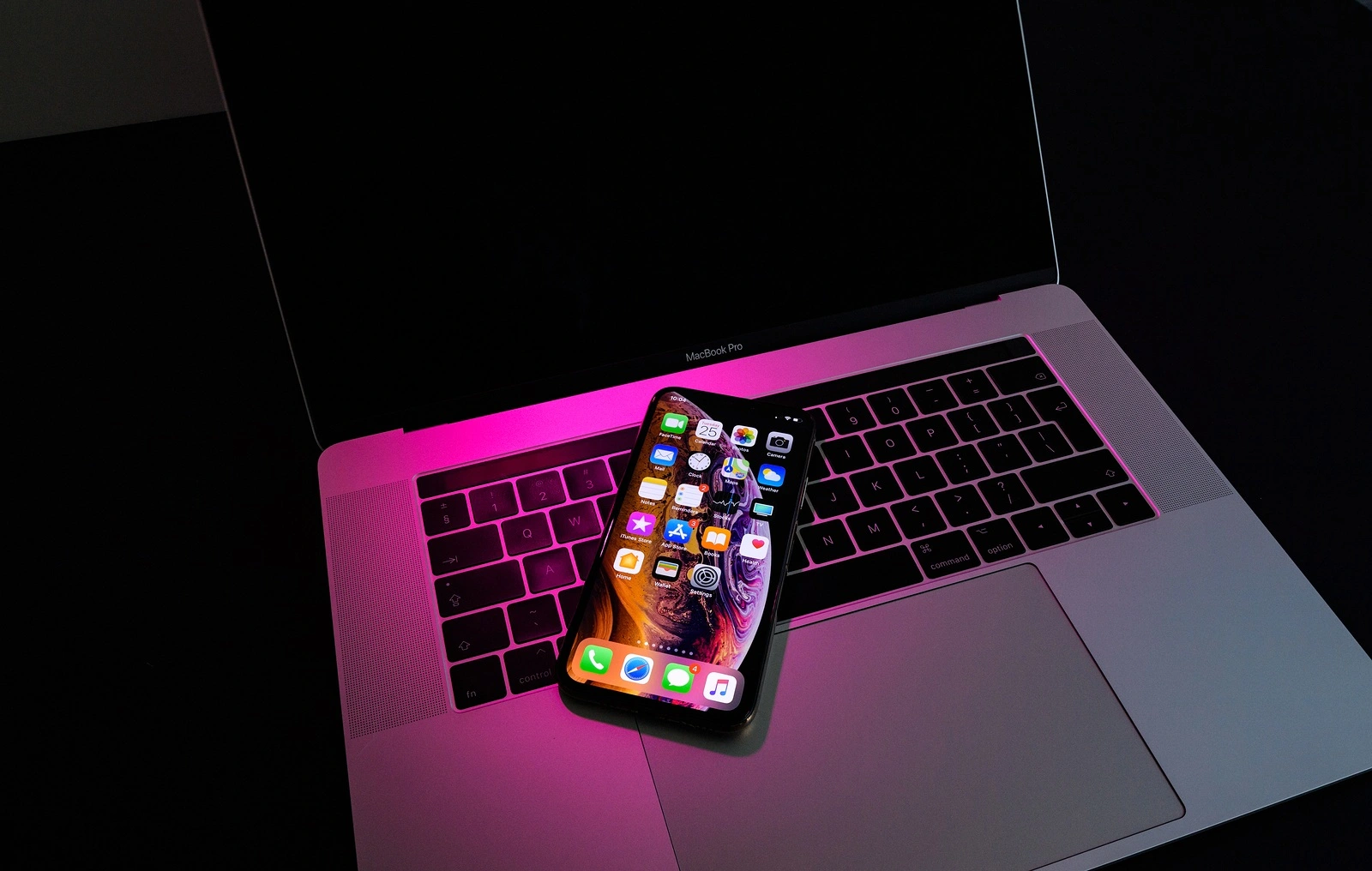 PARIS, FRANCE - SEP 25, 2018: New iPhone Xs and Xs Max smartphone model by Apple Computers close up. Newest golden Apple Iphone on pink magenta light on Macbook Pro 15 laptop keyboard