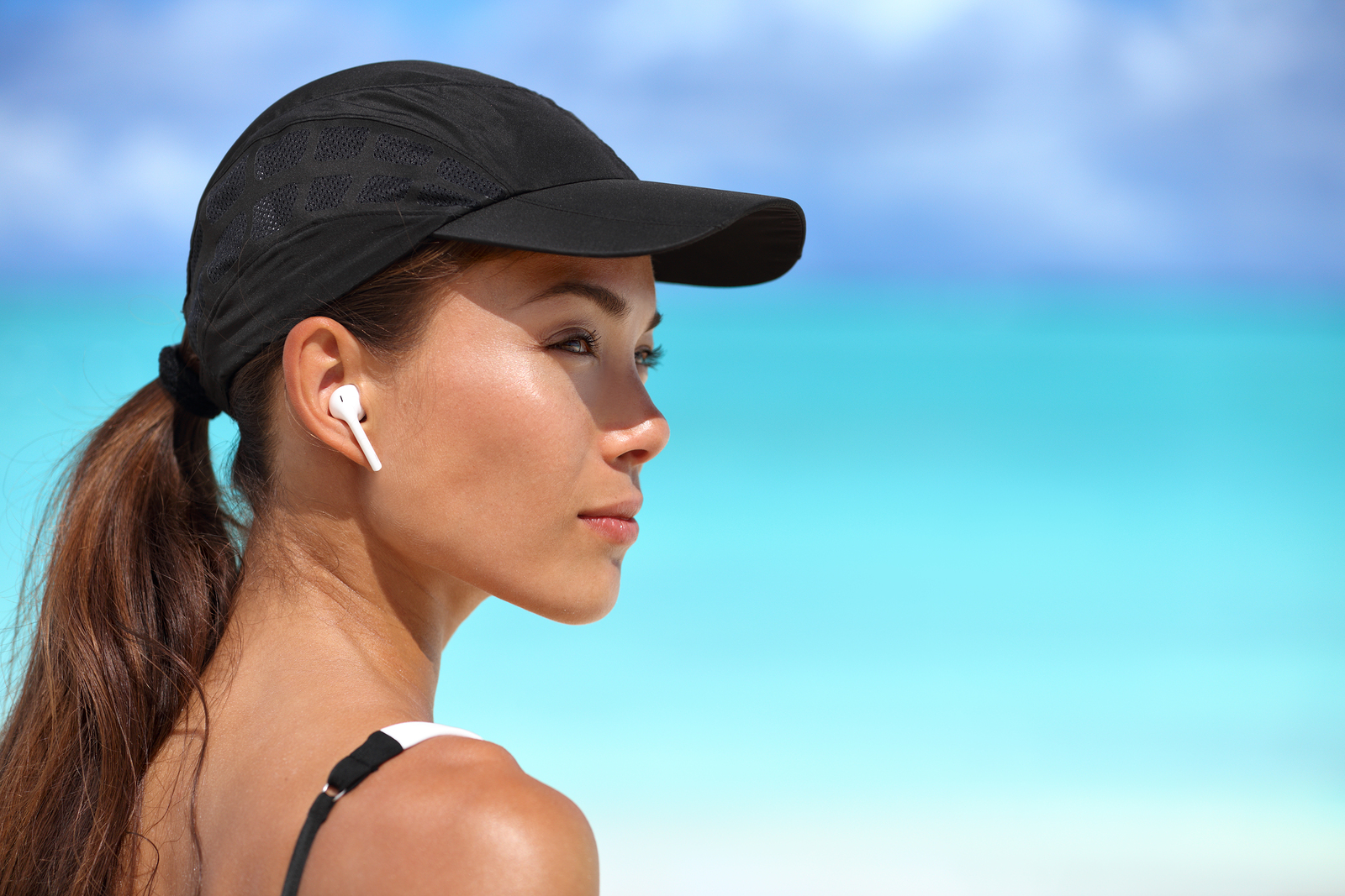 Wireless earbuds running woman on fitness workout. Active lifestyle athlete listening to smartphone music phone app with in-ear gear on beach. Asian woman healthy and active on summer vacation.