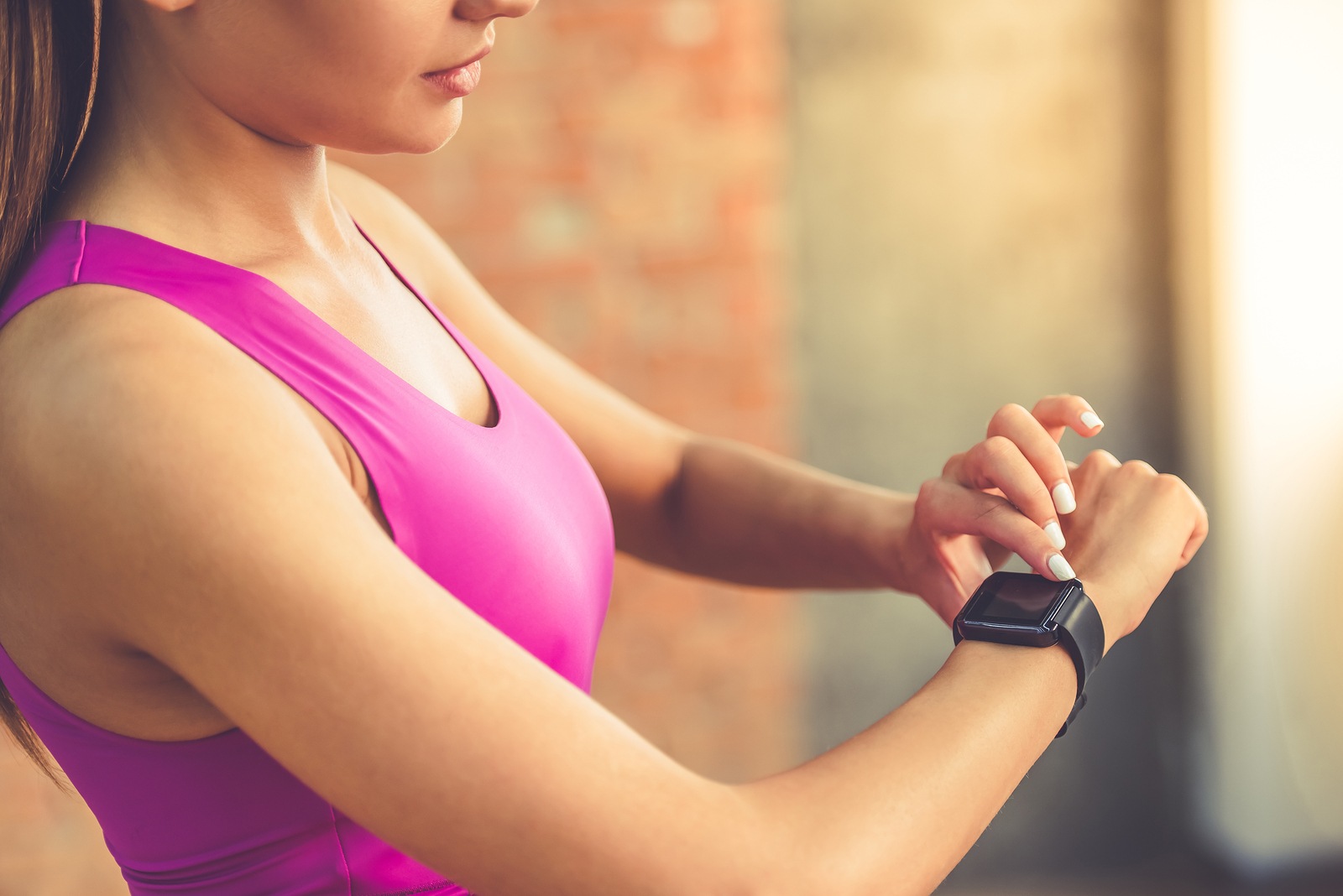 Cropped image of beautiful sports girl is switching on her Fitbit before training while standing in fitness hall