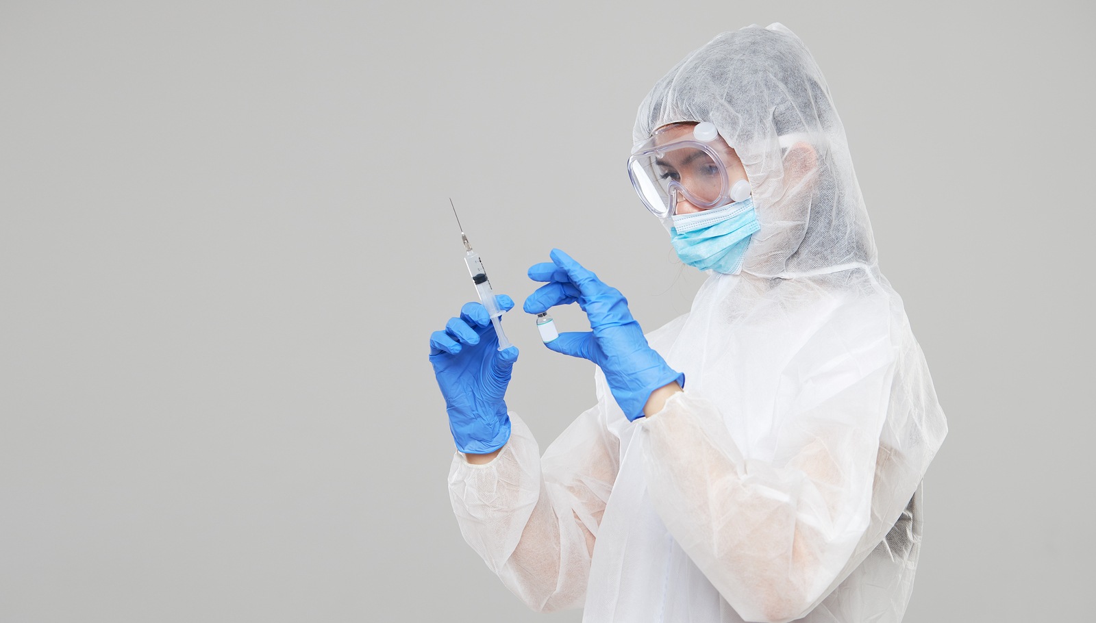 Biological hazard. Epidemic of the Chinese coronavirus. An Asian woman in a protective suit and mask holds an injection syringe and vaccine. Vaccine from flu, coronavirus, ebola, TB.
