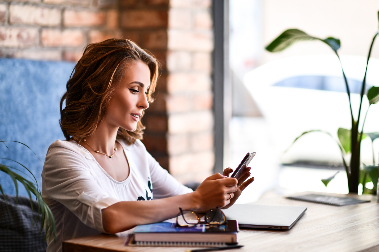 Charming woman with beautiful smile reading good news on mobile phone while resting in coffee shop, happy Caucasian female watching her photos on cell telephone while relaxing in cafe during free time