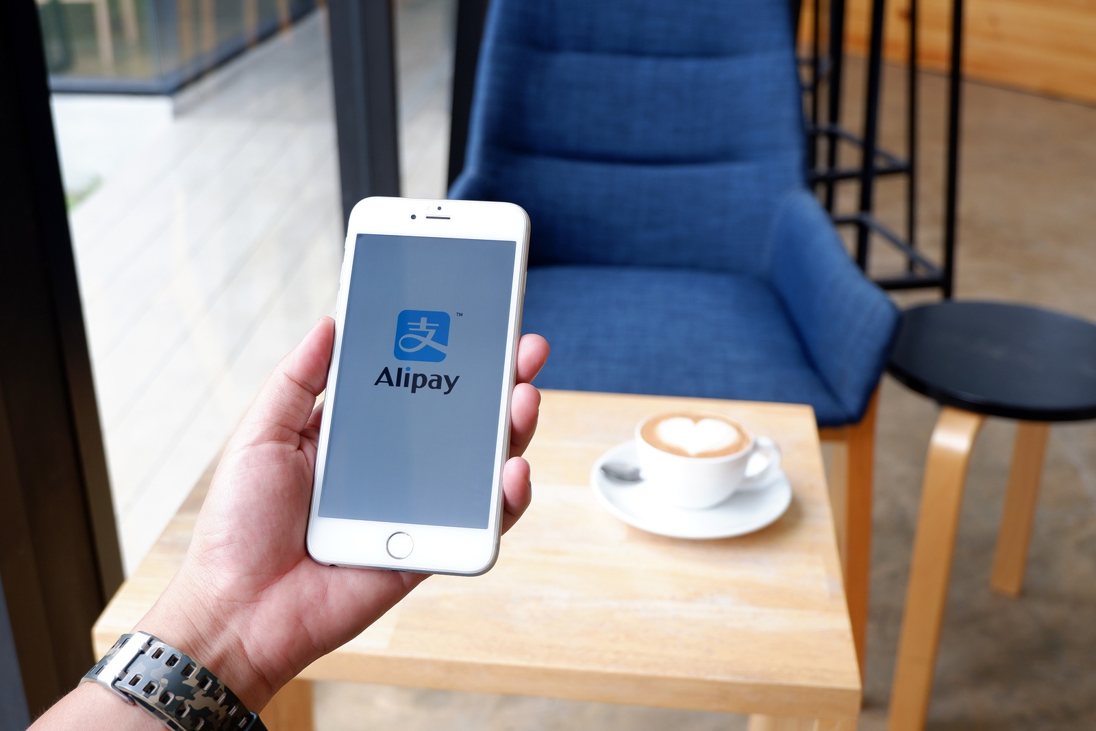 A man sitting in cafe holding mobile with alipay screen