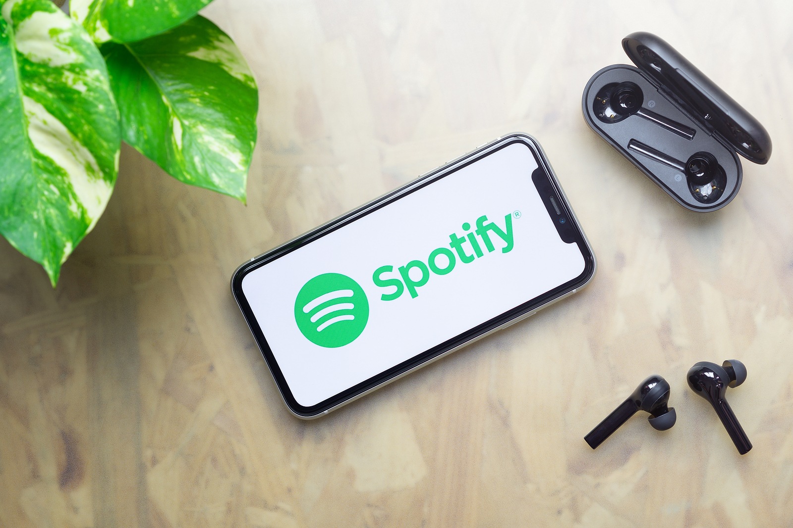 Bangkok, Thailand - July 3, 2020: Apple Iphone 11 with Spotify logo on display, bluetooth headphones with case, green plant on working table background. Flat lay top view