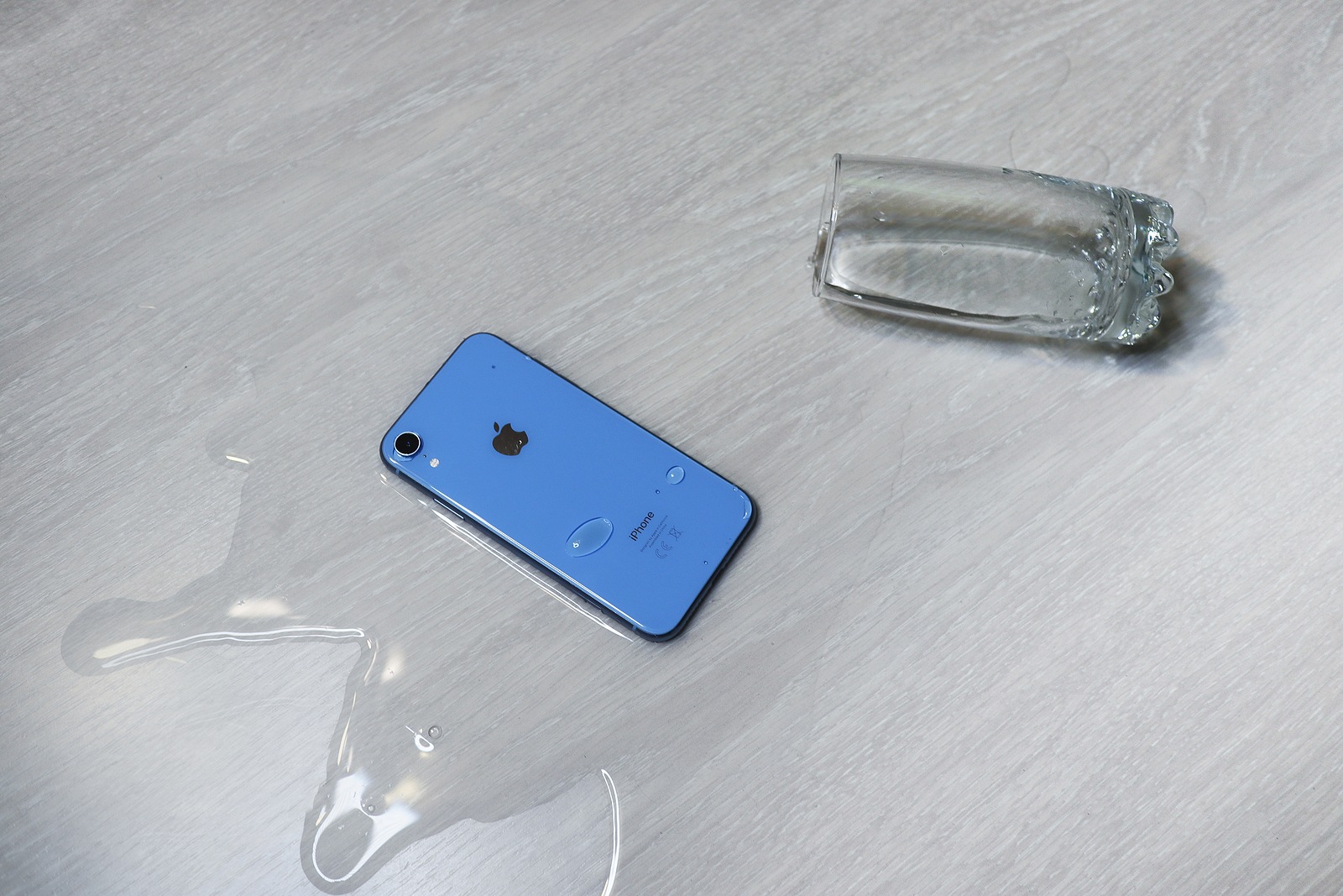 Saint-Petersburg/Russia - 11.11.19: Wet smartphone flooded. Water flows from overturned spilled glass to gadget. Water resistance, crash test. Waterproof of Apple iPhone XR. Inaccurate exploitation.