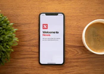 Anapa, Russia - October 13, 2018: iPhone X with news applications on the screen and background wooden desk. iPhone is created and developed by the Apple inc.