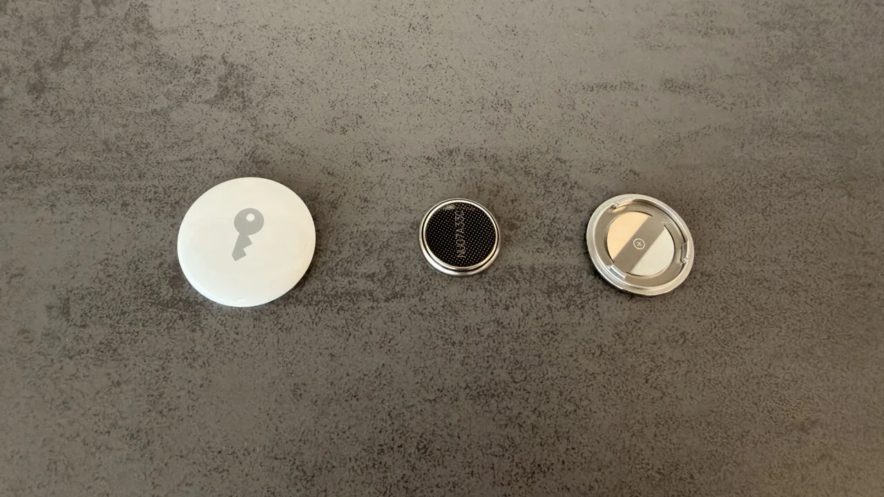 Replacing the AirTag battery: opened AirTag, removed CR2032 coin cell and the stainless steel cover side by side on a grey surface