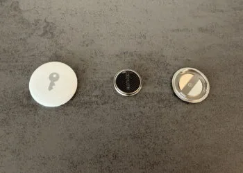 Replacing the AirTag battery: opened AirTag, removed CR2032 coin cell and the stainless steel cover side by side on a grey surface