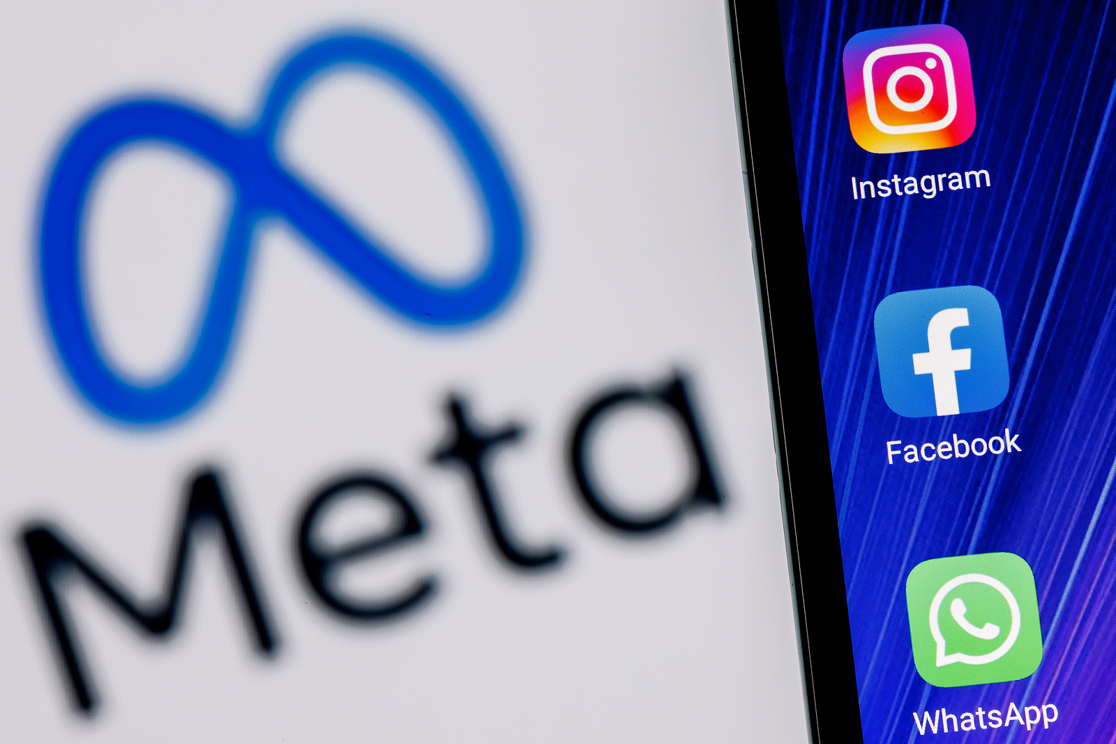Kazan, Russia - Oct 28, 2021: Facebook changes its name to Meta. Smartphone with Facebook, Whatsapp and Instagram app icon on the background of Meta logo.