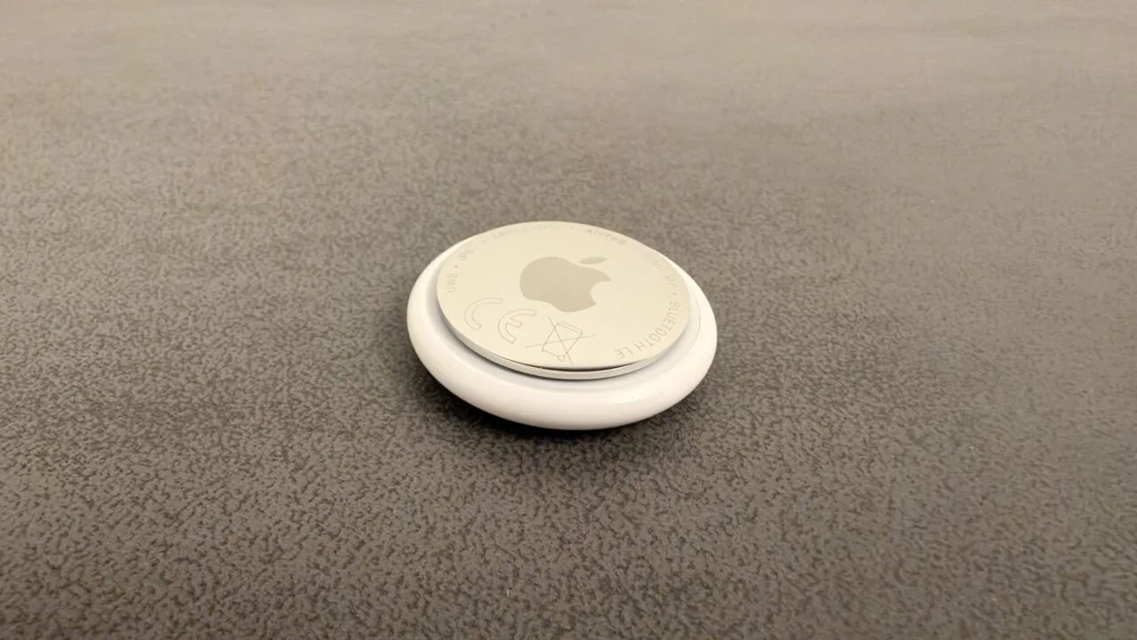 Apple AI pin: an AirTag on a grey surface used as a size comparison