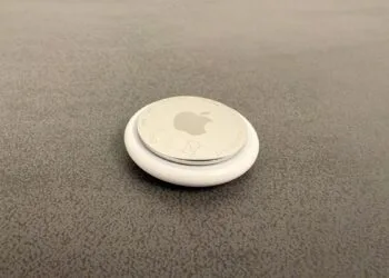 Apple AI pin: an AirTag on a grey surface used as a size comparison