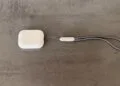 AirPods Pro 3 charging case with grey lanyard on a concrete surface, model without cameras