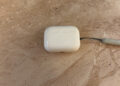 Closed AirPods Pro 3 charging case with lanyard on light marble, the model without cameras