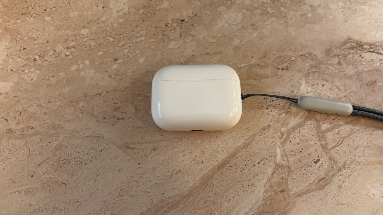 Closed AirPods Pro 3 charging case with lanyard on light marble, the model without cameras