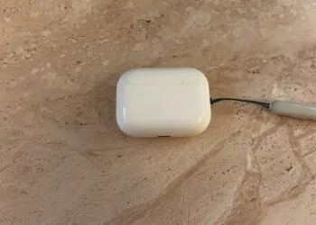 Closed AirPods Pro 3 charging case with lanyard on light marble, the model without cameras