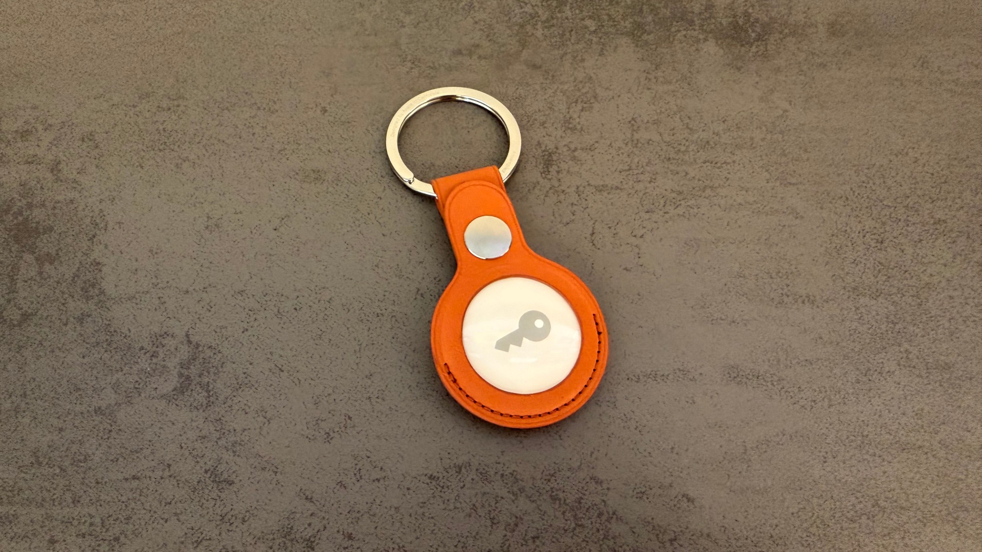AirTag 2 in a fuchsia FineWoven key ring on a dark surface, the type of tracker used in AirTag stalking
