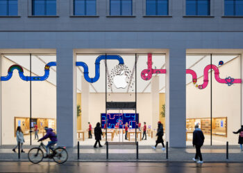 Symbolic image for Apple stock Jefferies: illuminated Apple Store on Rosenthaler Strasse in Berlin at dusk with passers-by outside