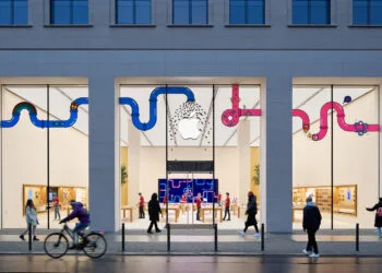 Symbolic image for Apple stock Jefferies: illuminated Apple Store on Rosenthaler Strasse in Berlin at dusk with passers-by outside