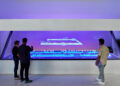 Three people study a holographic display of a production line at Apple's Houston training center