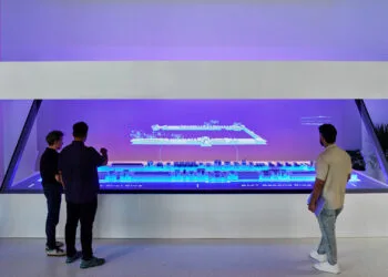 Three people study a holographic display of a production line at Apple's Houston training center