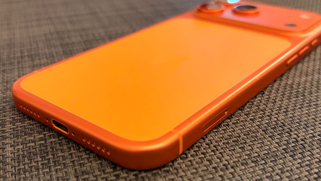 Glass panel set into the aluminium frame on the back of an iPhone 17 Pro Max in Cosmic Orange, whereas the iPhone 20 glass design is said to wrap the glass around the edges