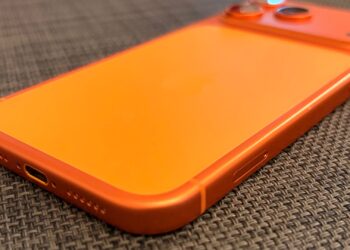 Glass panel set into the aluminium frame on the back of an iPhone 17 Pro Max in Cosmic Orange, whereas the iPhone 20 glass design is said to wrap the glass around the edges