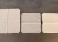 Three Apple polishing cloths side by side on a grey surface, the Apple Vision Pro cloth on the left, the 2026 Apple polishing cloth in the middle and the 2021 version on the right