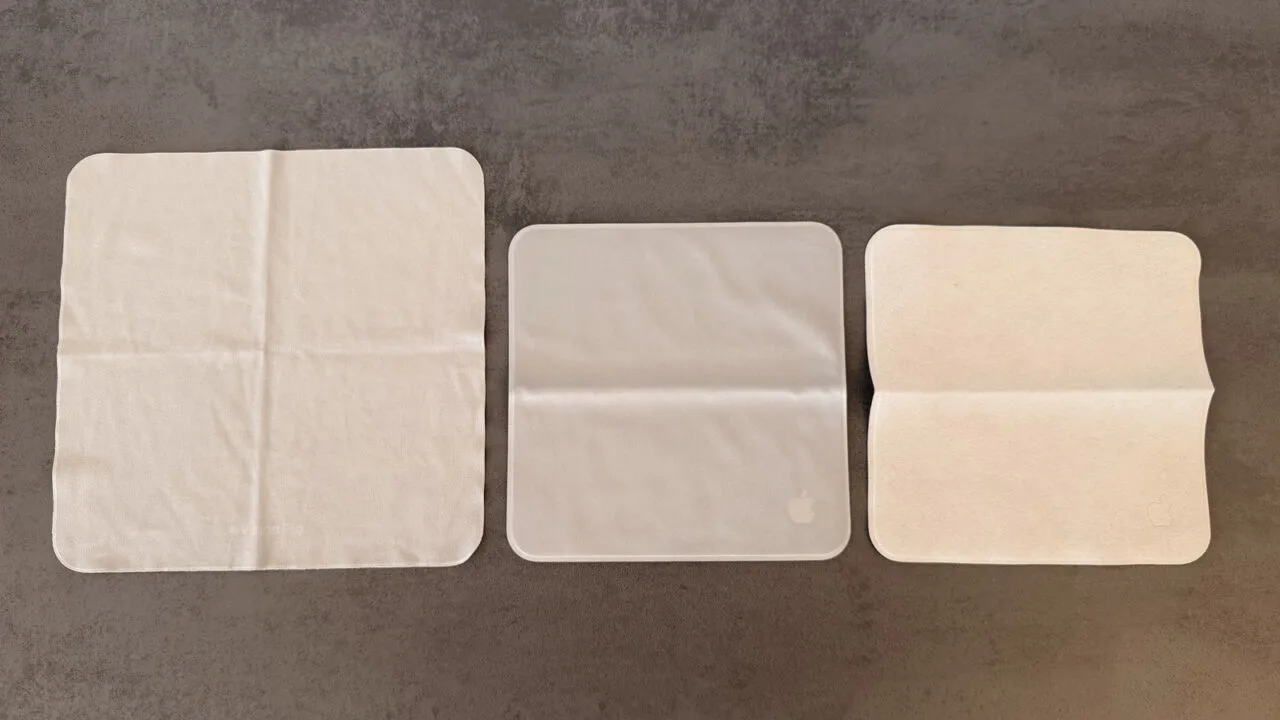 Three Apple polishing cloths side by side on a grey surface, the Apple Vision Pro cloth on the left, the 2026 Apple polishing cloth in the middle and the 2021 version on the right