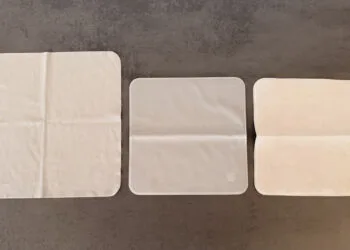 Three Apple polishing cloths side by side on a grey surface, the Apple Vision Pro cloth on the left, the 2026 Apple polishing cloth in the middle and the 2021 version on the right