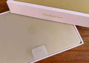 Half-opened box of the MacBook Neo in Citrus, the device still resting in its protective sleeve inside the packaging