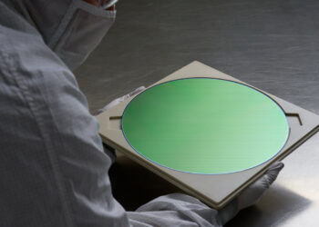 Worker in a cleanroom suit holding a semiconductor wafer of the kind TSMC also produces for iPhone 18 Pro chips