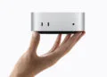 Mac mini M6 in silver held in a hand, front with two USB-C ports visible