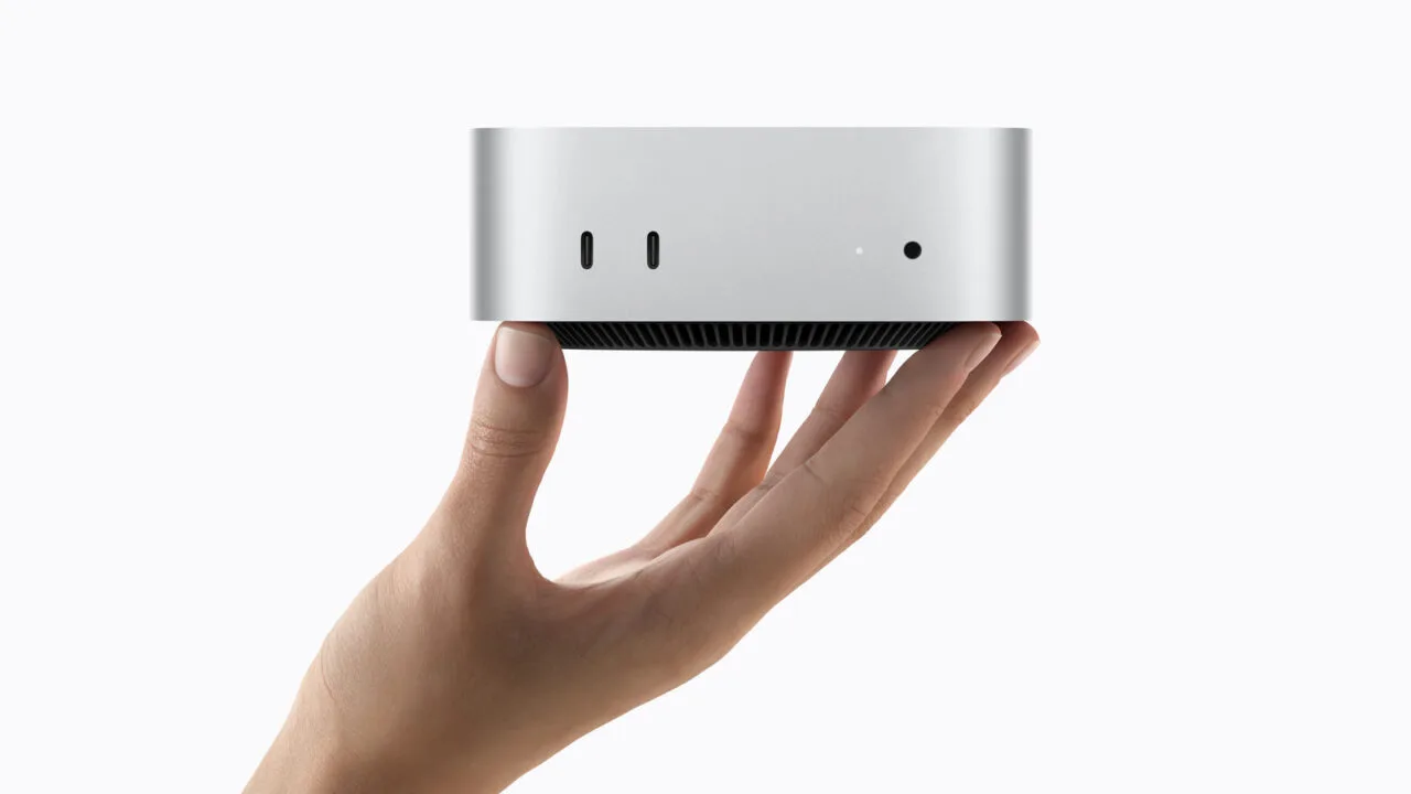 Mac mini M6 in silver held in a hand, front with two USB-C ports visible
