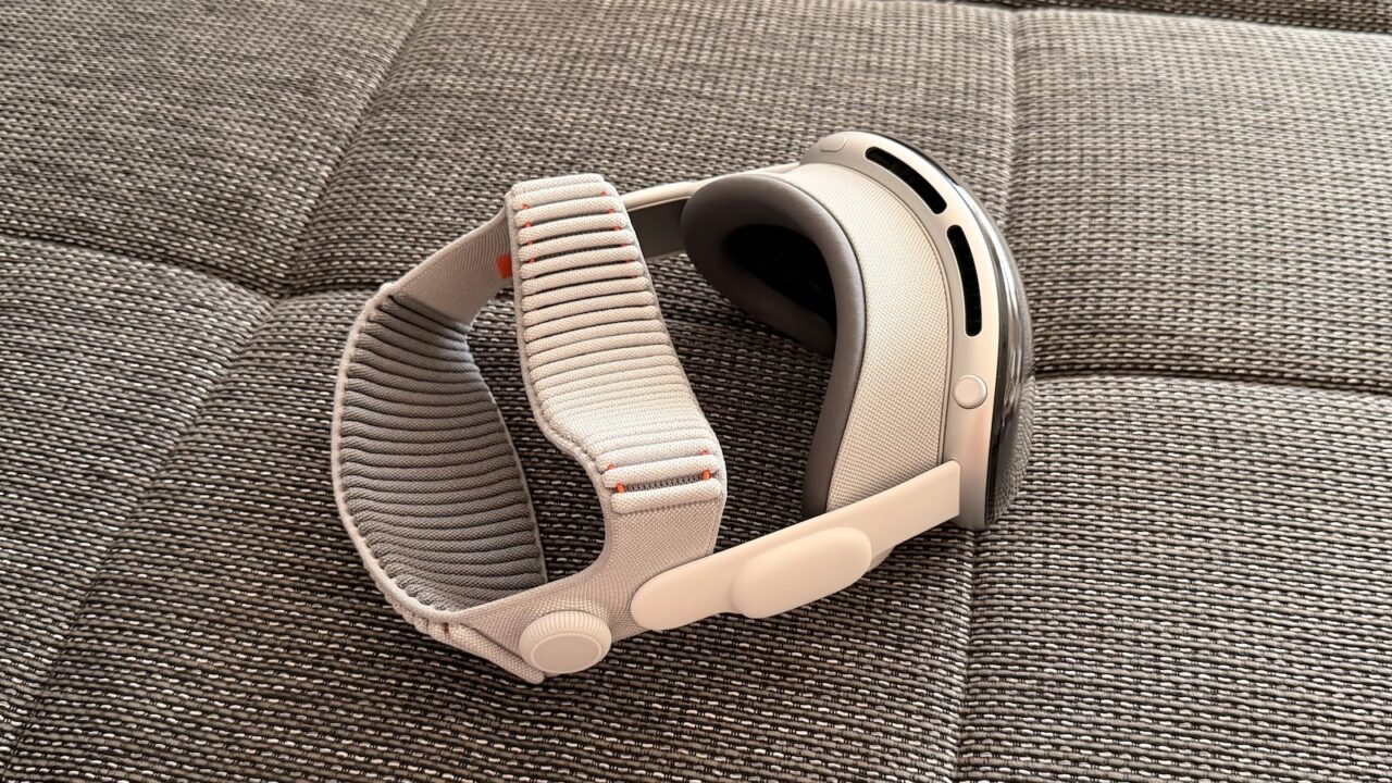 Apple Vision Pro with light Dual Knit Band resting on its side on a grey woven sofa surface