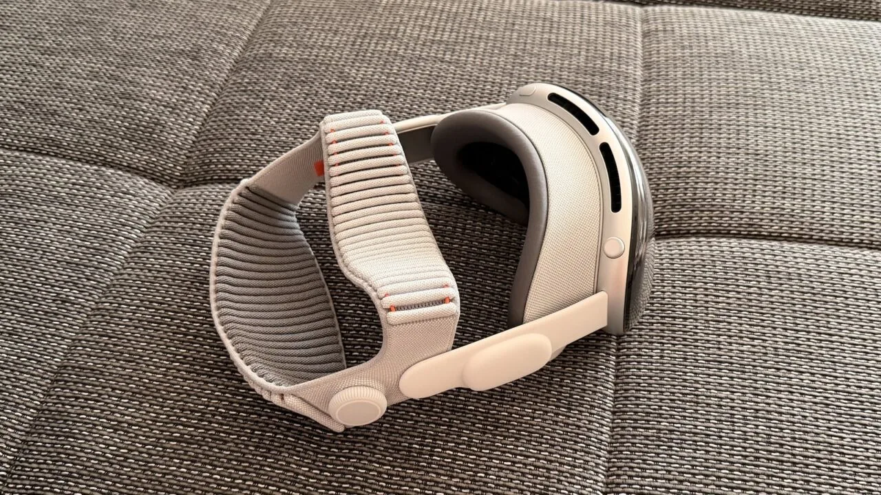 Apple Vision Pro with light Dual Knit Band resting on its side on a grey woven sofa surface