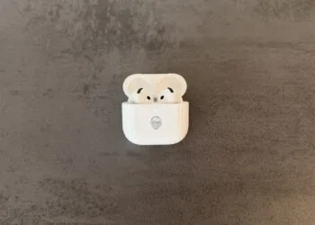 AirPods 5 in an open charging case with a Memoji engraving on a grey stone surface