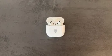 AirPods 5 in an open charging case with a Memoji engraving on a grey stone surface