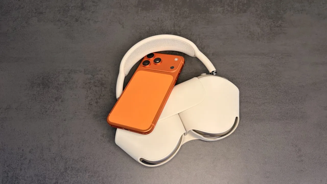 Adjusting the AirPods equalizer: orange iPhone resting on AirPods Max in their case on a grey surface
