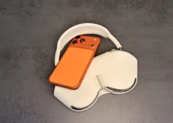 Adjusting the AirPods equalizer: orange iPhone resting on AirPods Max in their case on a grey surface