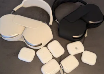 Several AirPods charging cases and two pairs of AirPods Max on a grey surface, illustrating AirPods firmware across models