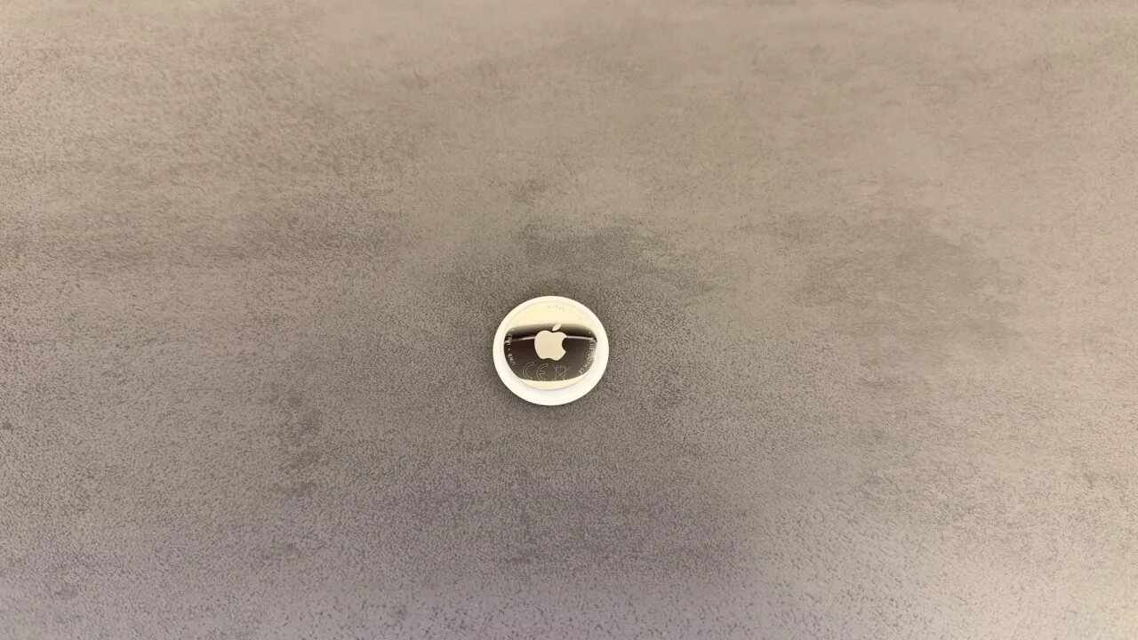 Apple AI pin: an AirTag on a grey surface used as a size comparison