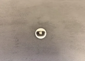 Apple AI pin: an AirTag on a grey surface used as a size comparison