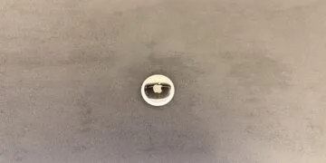 Apple AI pin: an AirTag on a grey surface used as a size comparison
