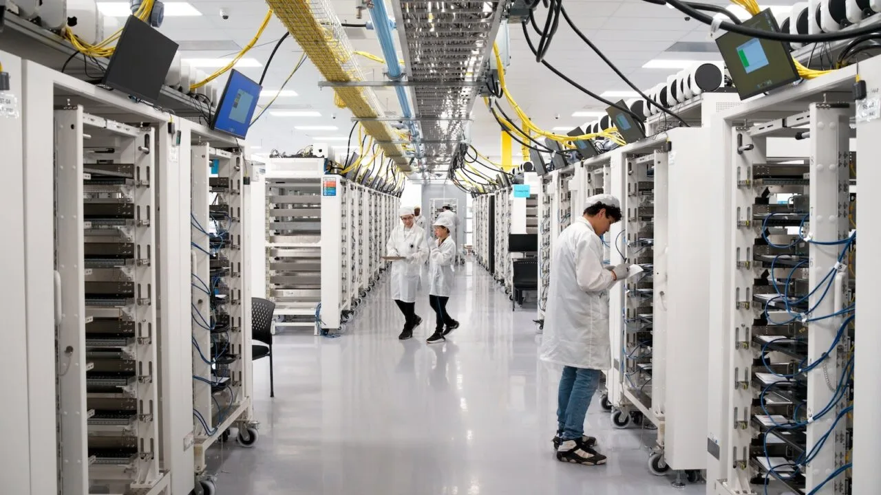 Apple AI server: aisle between server racks at Apple's Houston facility, staff in protective clothing checking the units