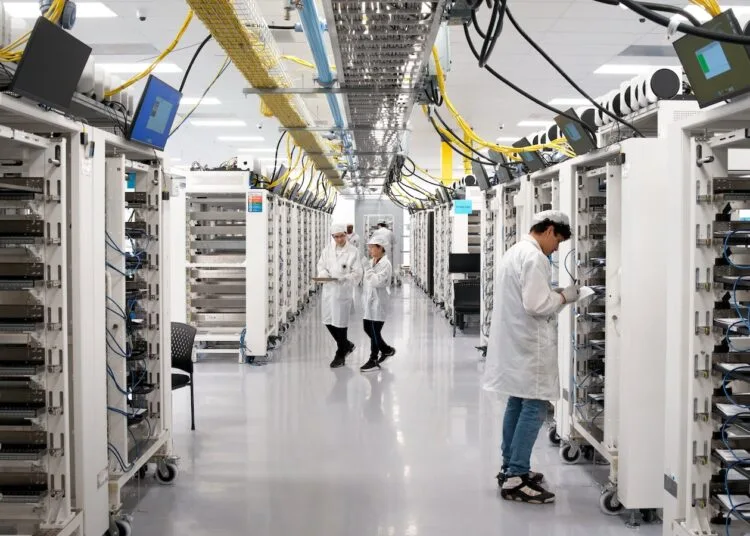Apple AI server: aisle between server racks at Apple's Houston facility, staff in protective clothing checking the units